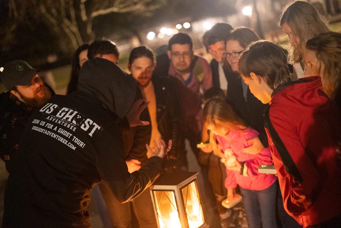 Guests gather around a glowing lantern on a nighttime ghost tour